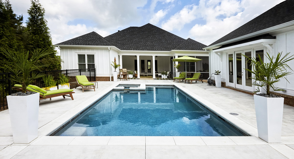 Backyard inground pool and spa with lounge chairs and a white farmhouse